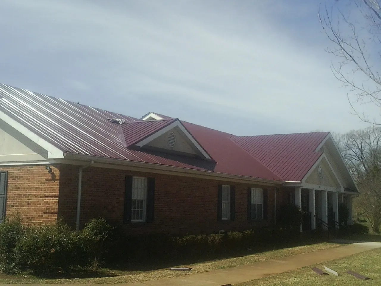 Red metal roof with gabled entries on a long brick building, from a Hail Damage Roof Repair job in Tehuacana