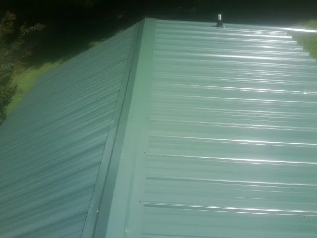 New green metal panels meeting at the ridge of a roof — Flat Roof Repair work by our crew in Tehuacana