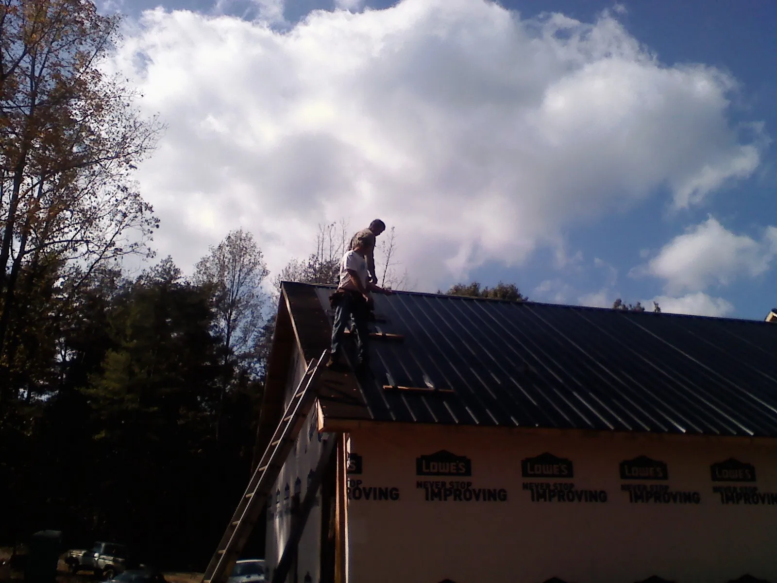 Roofer fastening dark metal panels high against a cloudy sky, from a Roof Inspection job in Tehuacana