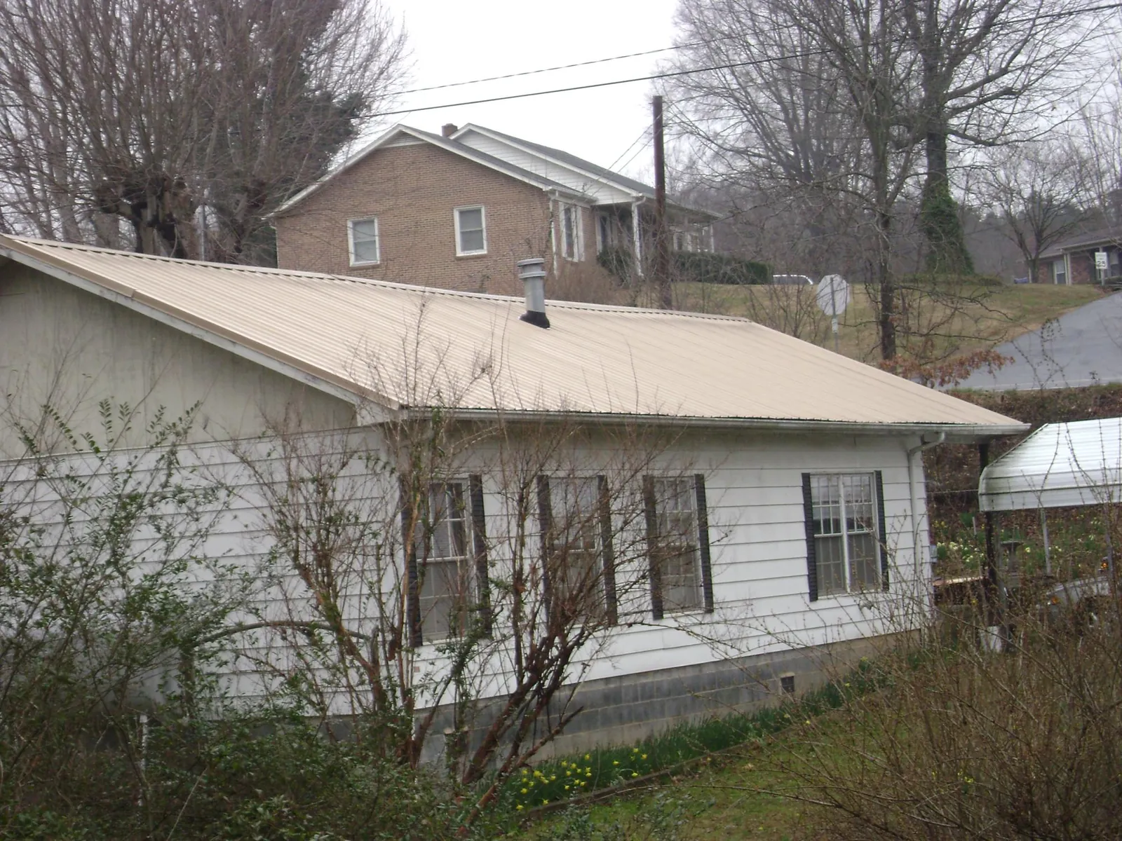 Tan metal roof on a white sided house set into a hillside — Commercial Roofing by Roofing Brothers in Tehuacana