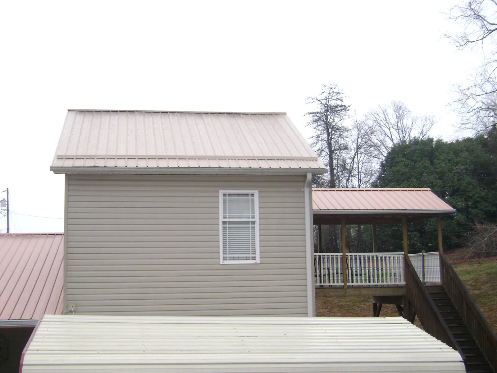 Tan metal roofs on a two story addition and attached porch, from a Roof Replacement job in Tehuacana